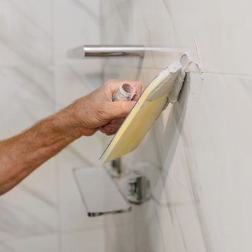 Hand applying grout to bathroom tiles with a float tool.