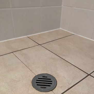 Cracked bathroom floor tile near a drain on tiled walls and floor.