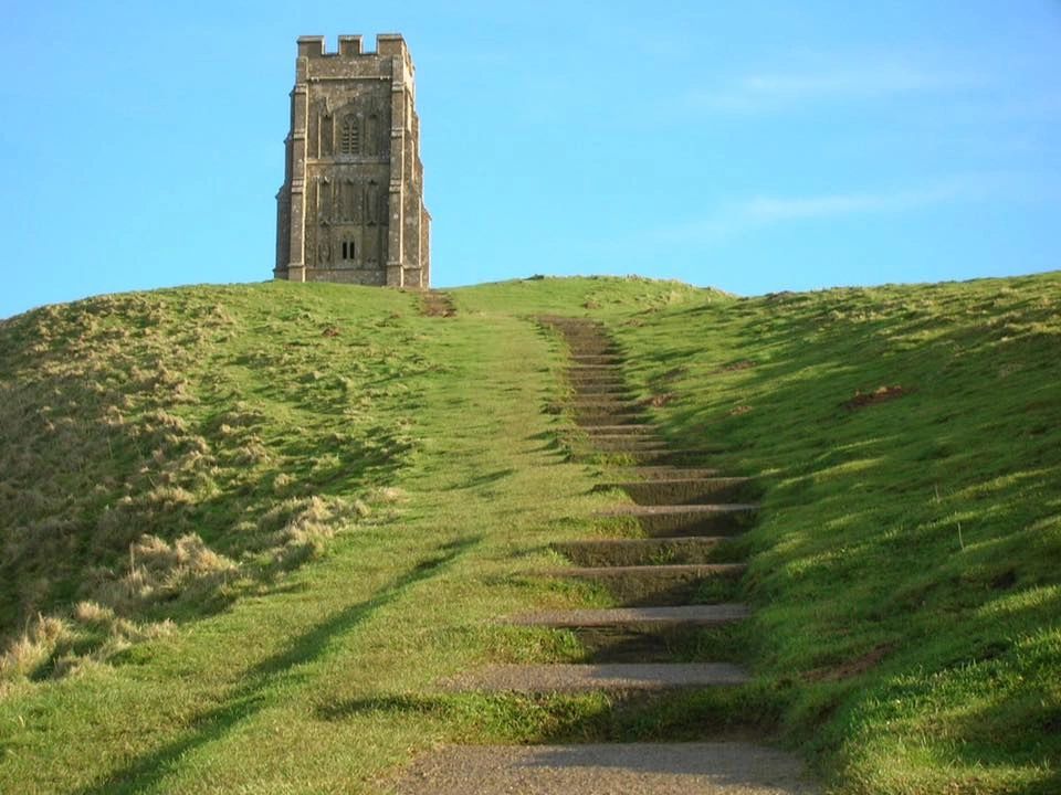 Stone tower on a grassy hill under clear blue sky.