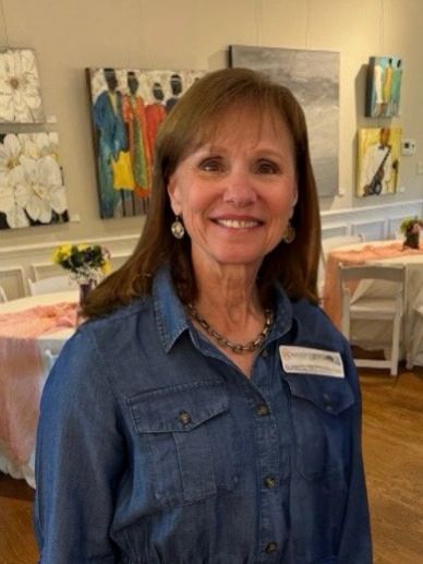 Smiling woman in a denim shirt at an art-filled room event.