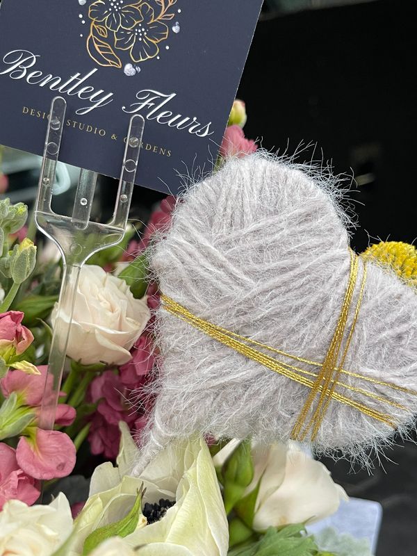 gray yarn heart in floral arrangement of white garden roses, pink stock, and bentley fleurs logo