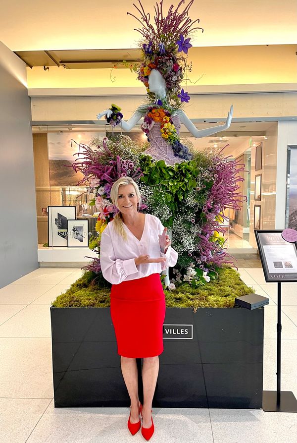 Designer Kelley holding Glass Award in front of floral mannequin
