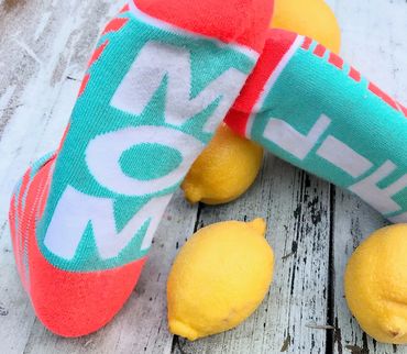Socks in orange and mint green with lemons with the word mom life on the soles of the socks