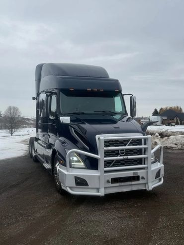 Black Volvo semi-truck with a protective front grille parked on a snowy road.