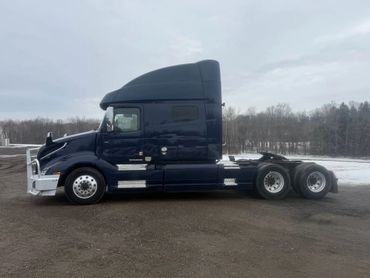 Dark blue semi-truck parked on a dirt area with a snowy background.