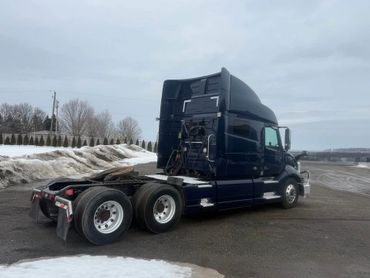 A dark blue semi-truck parked on a snowy roadside under a cloudy sky.
