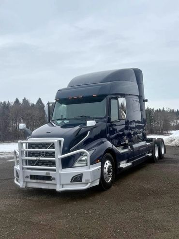 A dark blue Volvo semi-truck with a white front grille guard parked outdoors.