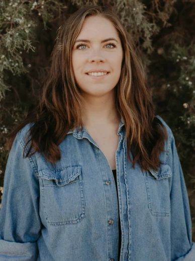 Woman in denim jacket smiling outdoors.