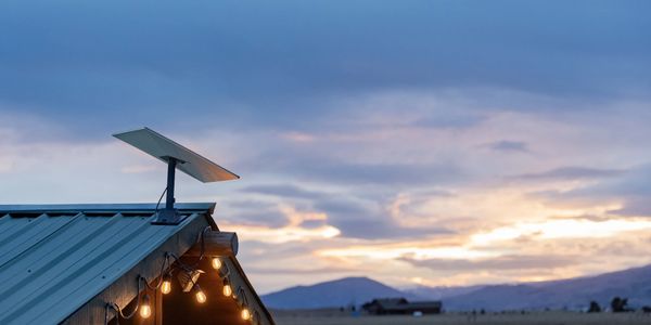 Solar panel on a rooftop with string lights during sunset in a rural area.
