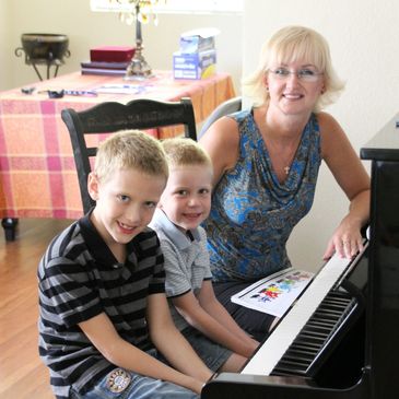 Olga Johnson, traveling piano teacher sitting at piano with 2 of her students in Orange County, CA