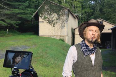 Man in hat with camera filming outdoors.