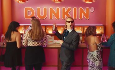 Man holding Dunkin' cup at counter with four women.