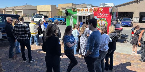 People gather outside near a colorful food truck on a sunny day.