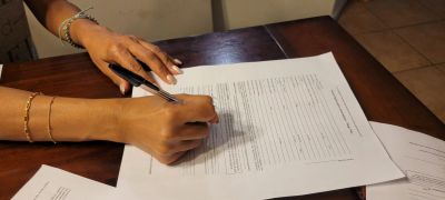Person filling out a form with a pen at a wooden desk.