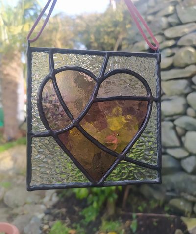 Stained glass heart hanging outdoors with a stone wall background.
