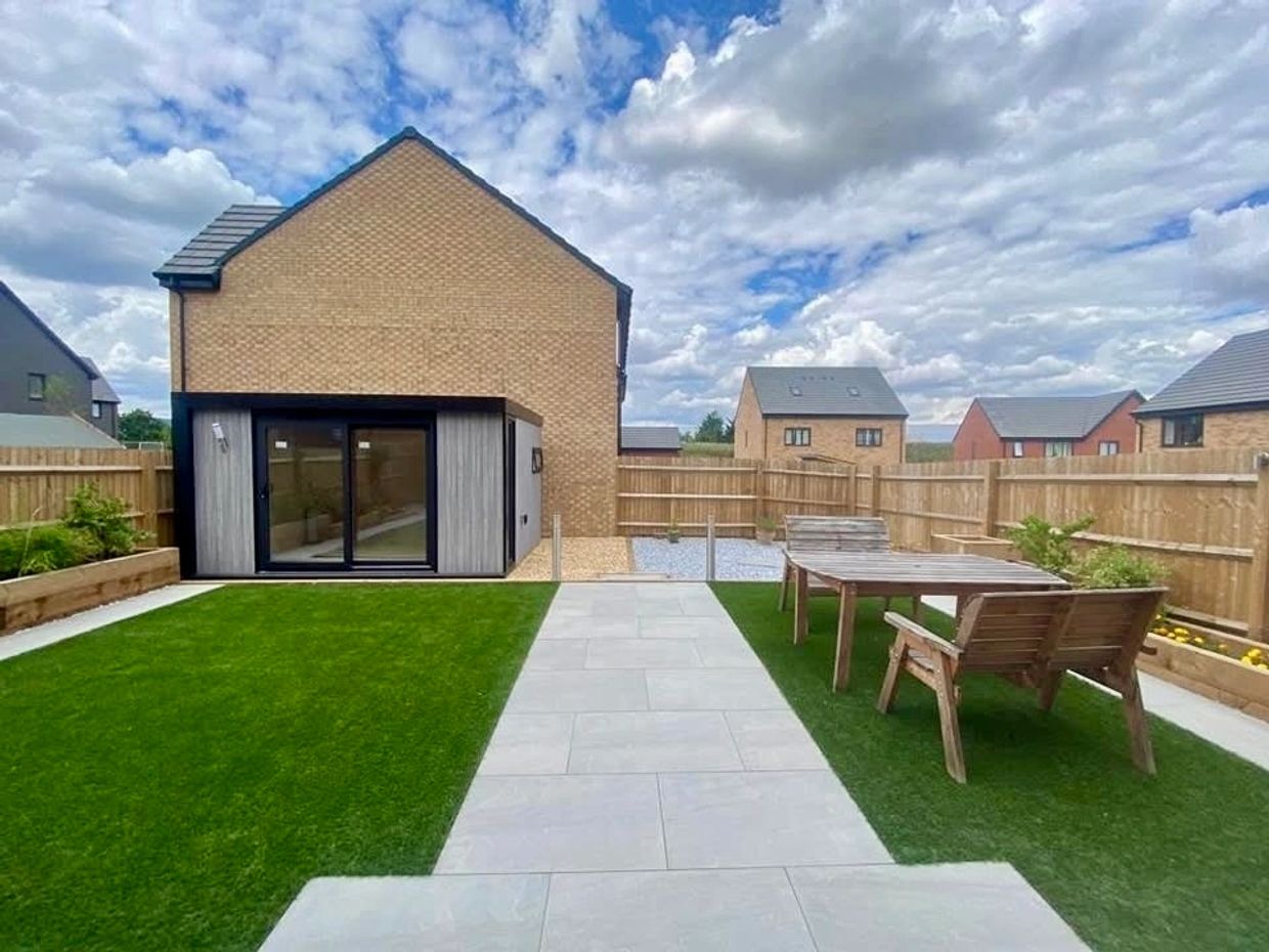 Backyard with wooden furniture and modern house under cloudy sky.