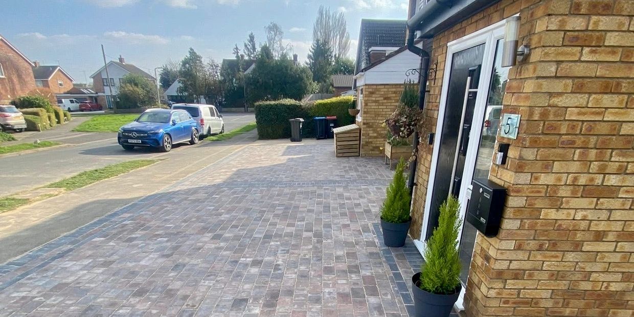 A clean brick driveway in front of a house with two potted plants.