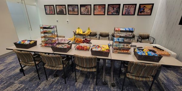 A table with assorted snacks and fruits in baskets and racks in a meeting room.