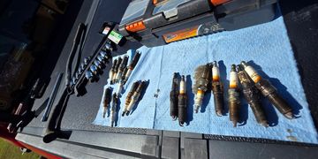 Used spark plugs laid out on a blue cloth with tools nearby.