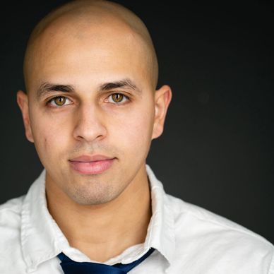 Close-up portrait of a bald man with hazel eyes in a white shirt and loosened tie.