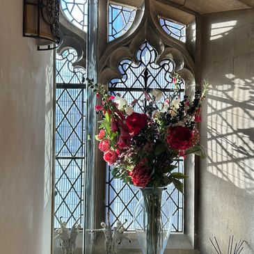 Bouquet of vibrant flowers in front of a gothic-style window with sunlight.