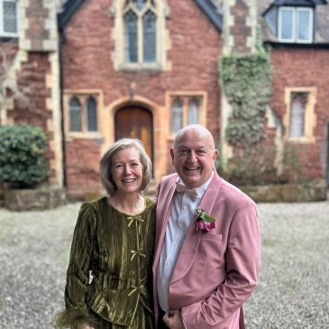 Happy couple posing outdoors in front of a brick building.