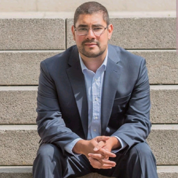 Man in a suit sitting on concrete steps looking at the camera.