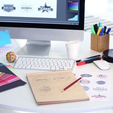 Creative workspace with logo designs, color swatches, and drawing tools on a white desk.