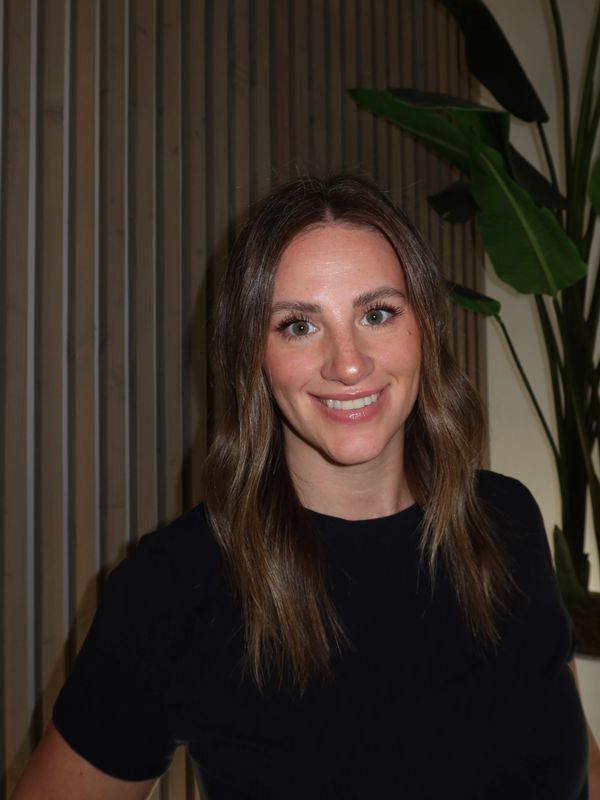 Smiling woman with brown hair in a black shirt standing indoors.