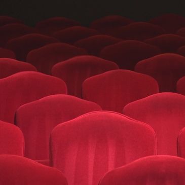 Rows of empty red theater seats in dim lighting.