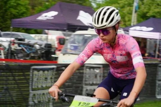 Cyclist in pink jersey and helmet racing on a bike outdoors.