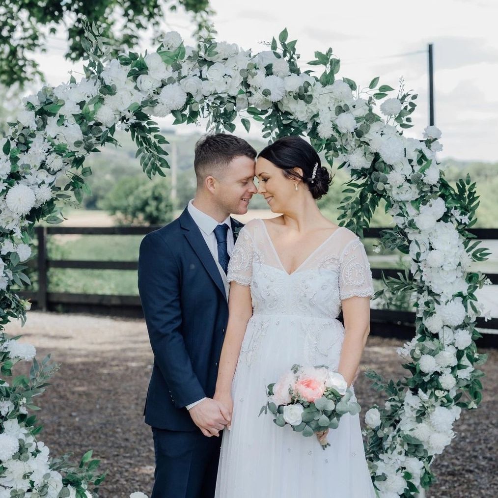 Couple in wedding attire under a floral arch.