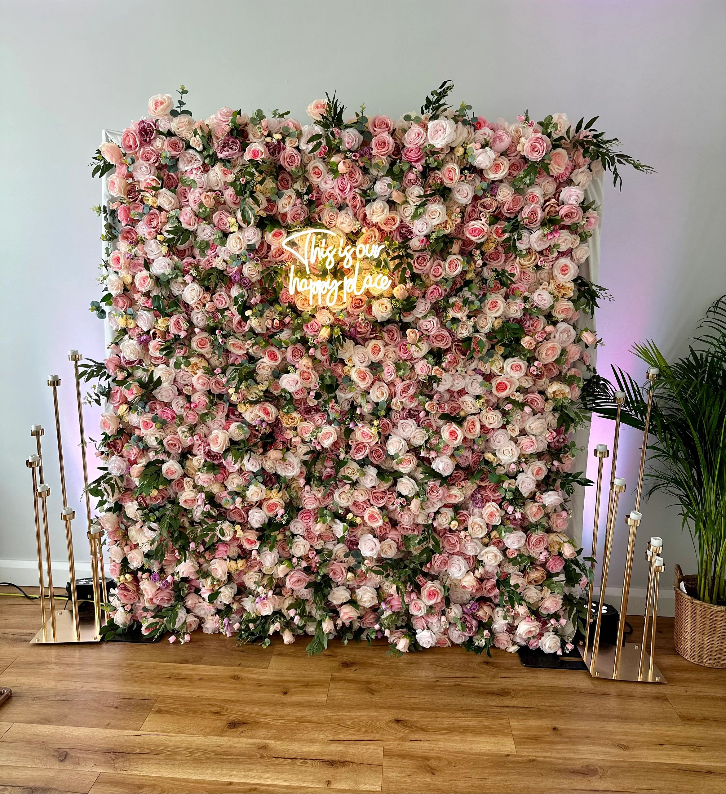 Floral wall with a neon sign and gold candle holders.