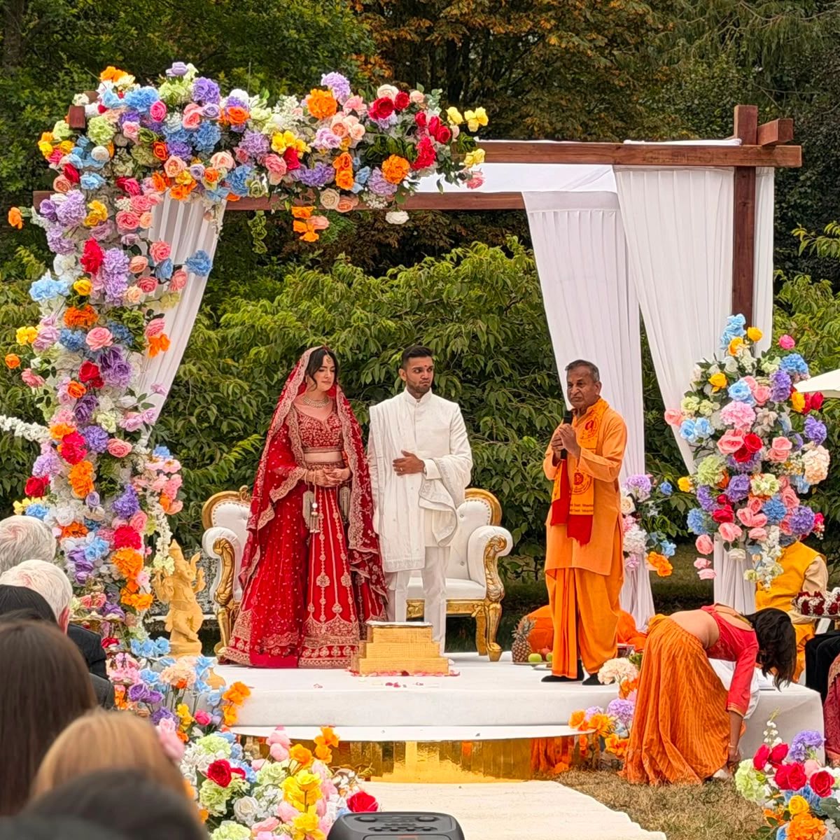 A couple in traditional attire at a vibrant outdoor wedding ceremony.