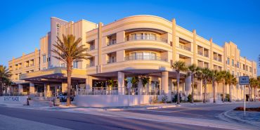 Modern hotel building with palm trees under blue sky.