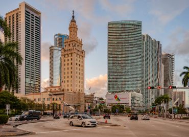 City street with tall buildings and palm trees at sunset.