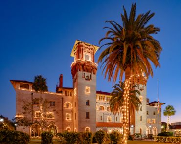 Historical building illuminated at dusk with palm trees.