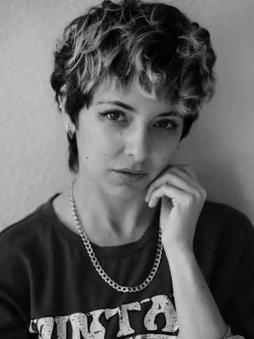 Black and white portrait of a young person with short curly hair and a chain necklace.