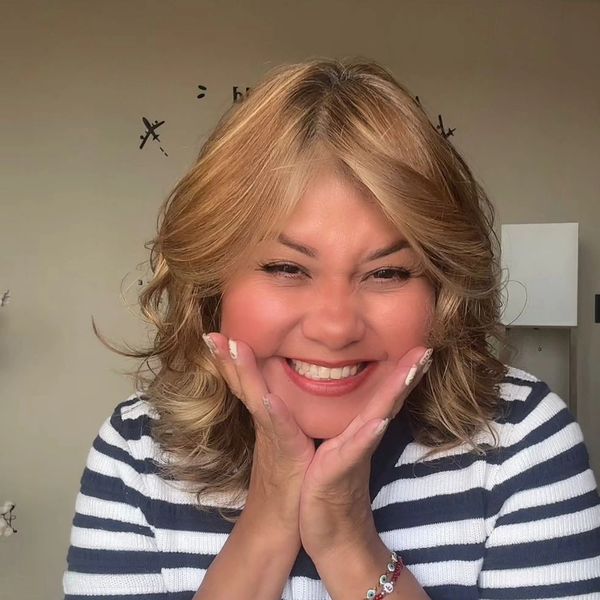 Woman smiling joyfully with hands on her cheeks in a striped shirt.
