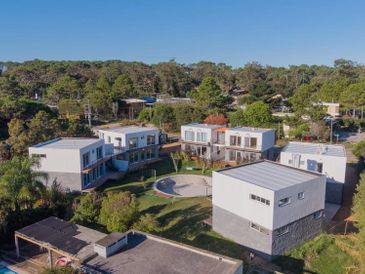 Modern white houses with flat roofs in a green suburban area under a clear blue sky.