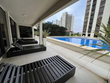 Modern outdoor lounge chairs near a rooftop pool with city view.