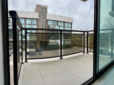Modern balcony with glass railing overlooking a parking area and building.