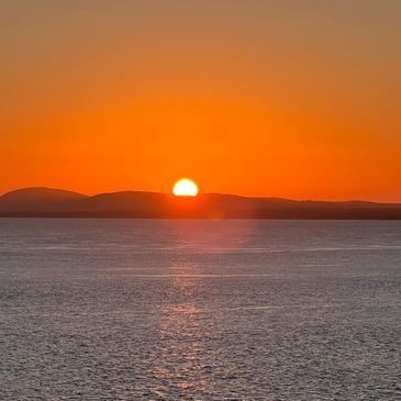 Sun setting behind silhouetted hills over a calm body of water.