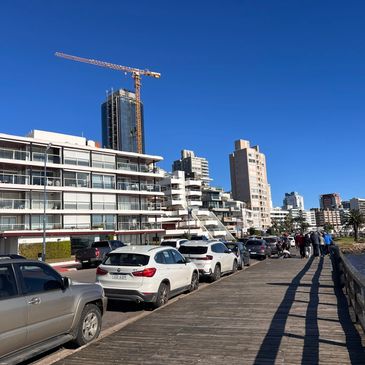 Waterfront with parked cars, modern buildings, and a construction crane under a clear blue sky.