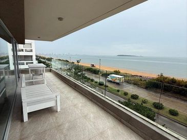 Spacious balcony with white furniture overlooking the beach and ocean.