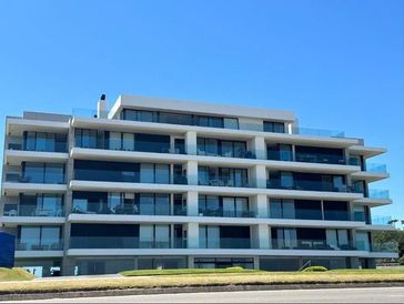 Modern multi-story apartment building with large glass balconies and a clear blue sky.