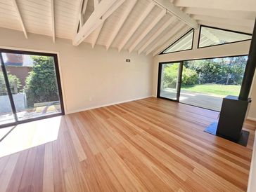 Bright room with wooden floor, white ceiling, and large glass doors opening to a garden.