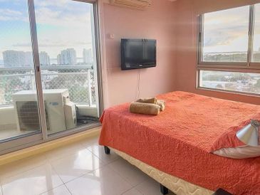 Cozy bedroom with orange bedding and city view through large windows.