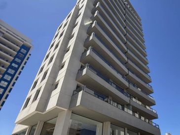 Tall modern apartment building with balconies against a clear blue sky.