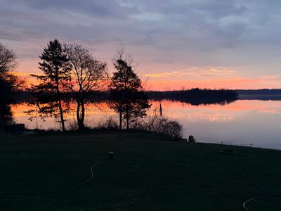 Sunset over a calm lake with silhouetted trees.